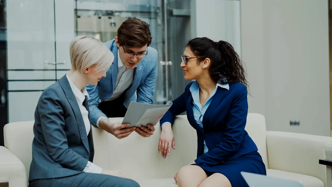 Three business people in suits discussing documents.