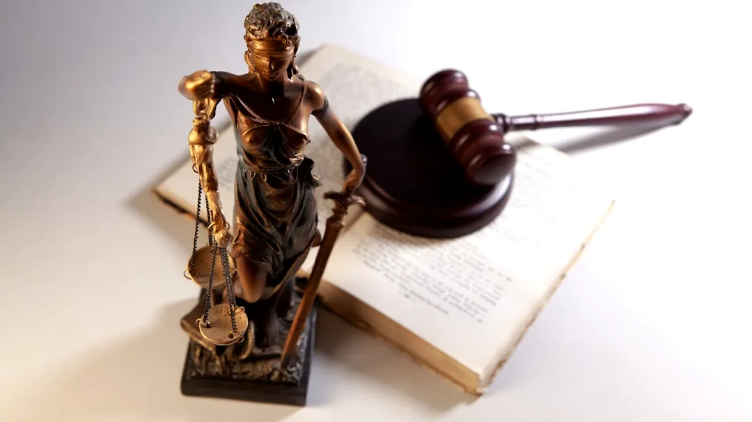 Statue of justice, gavel, and open book on table.